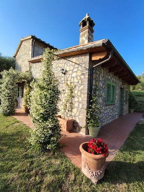 A stone house with a chimney, green shutters, and a brick pathway leading to the entrance.
