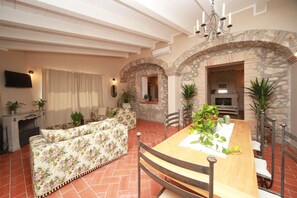 A dining area with a wooden table and chairs, surrounded by stone arches and potted plants.