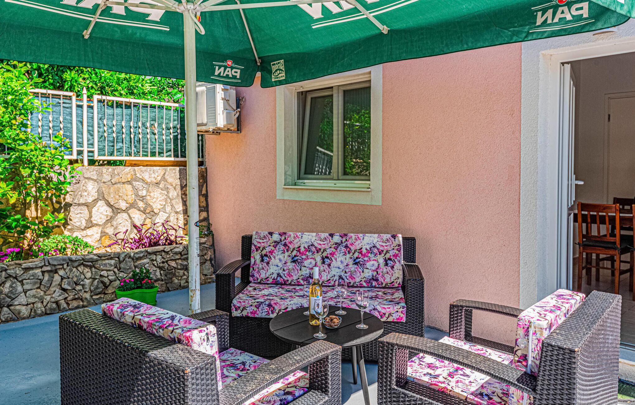 An outdoor seating area with wicker furniture and a table, under a green umbrella.