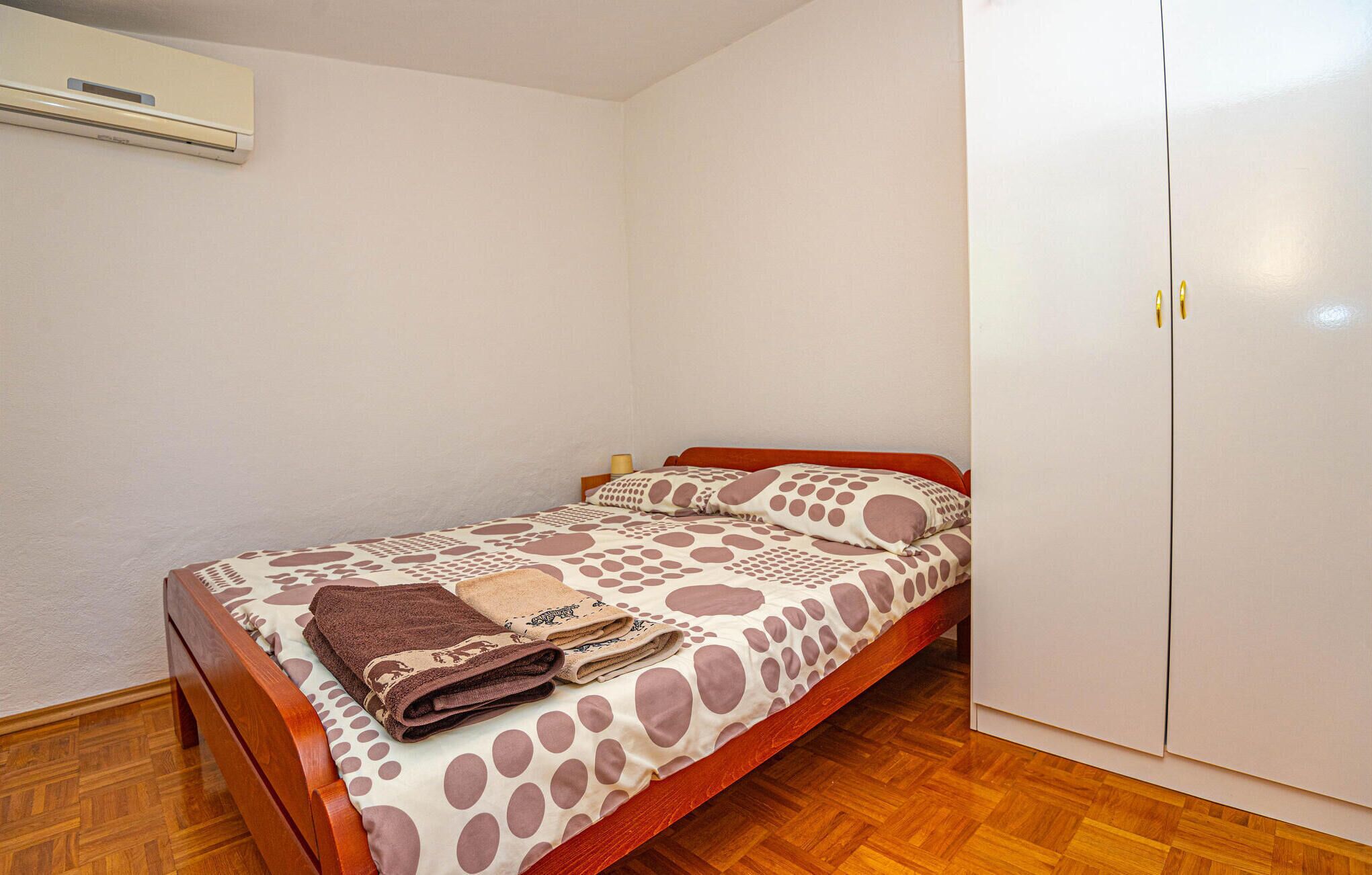 Ein Einzelbett mit einem Punkte-Bettbezug, einem Holz-Kopfteil und einem braunen Handtuch, das auf dem Bett gefaltet liegt.