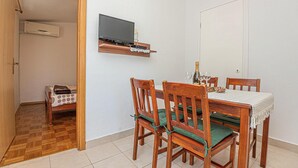 Ein Essbereich mit Holztisch und Stühlen, einem an der Wand montierten Fernseher und einer Tür im Hintergrund.