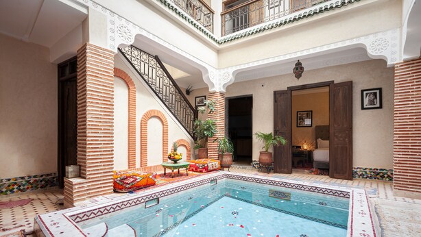 Zona de piscina con piso de baldosas, una escalera y un espacio de descanso con cojines.