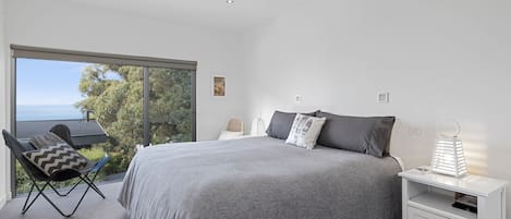 A bedroom with a large bed, a chair, a nightstand, and a view of the outdoors.