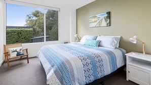 A bedroom with a large window, a bed with patterned bedding, a bedside table with a lamp, and a painting on the wall. - Seasoon Luxury Amongst The Treetops Ocean Views (Lorne)