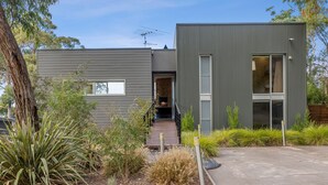 A modern two-story house with a flat roof, a visible chimney, and a small deck leading to the entrance. - Seasoon Luxury Amongst The Treetops Ocean Views (Lorne)