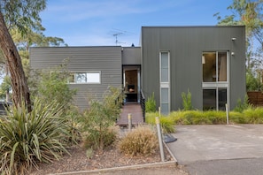 A modern two-story house with a flat roof, a visible chimney, and a small deck leading to the entrance. - Seasoon (Lorne)