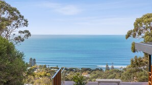 Vista sul mare da un balcone con ringhiera in legno, che si affaccia sull'oceano e su una zona residenziale con alberi e case.