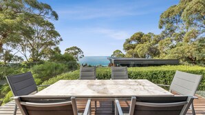 An outdoor dining area with a view of the sea, surrounded by trees and a modern building. - Seasoon Luxury Amongst The Treetops Ocean Views (Lorne)