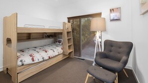 Un letto a castello con scrivania estraibile, una poltrona grigia, una lampada da terra e una finestra vista alberi.