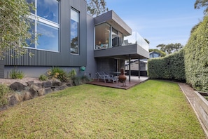 Une maison moderne à deux étages, dotée d’un toit plat, de grandes fenêtres et d’un patio couvert aménagé avec du mobilier d’extérieur.