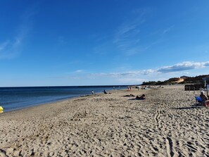 Una spiaggia sabbiosa con un cielo azzurro limpido, alcune persone e edifici sullo sfondo.
