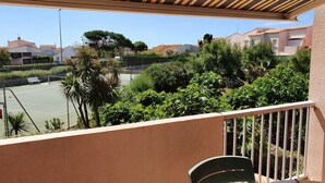 Ein Balkon mit Blick auf einen Tennisplatz, umgeben von Grünflächen und Wohnhäusern.