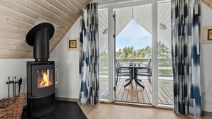 Ein gemütlicher Raum mit Kaminofen, einem Esstisch mit Stühlen und Blick ins Freie.