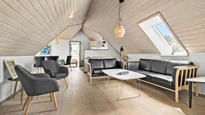 Ein modernes Loft mit schrägverdachter Decke, einem Essbereich mit Tisch und Stühlen, einer Couch und einer hängenden Leuchte.