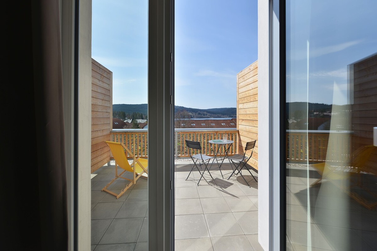 A balcony with a view of a hilly landscape, wooden furniture, and a glass door.
