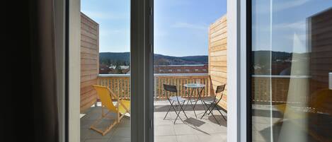 A balcony with a view of a hilly landscape, wooden railings, and a table with chairs.