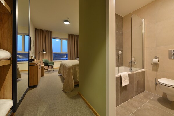 A hotel room with a bed, desk, chair, and a bathroom with a bathtub and toilet. - Hotel Element Lipno (Lipno nad Vltavou)