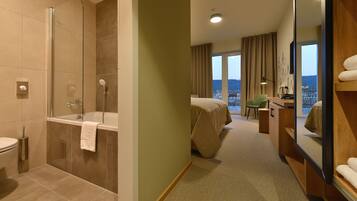 Une chambre d’hôtel équipée d’une douche, de toilettes, d’un lit, d’un bureau, d’une chaise et d’une grande fenêtre donnant sur la ville.