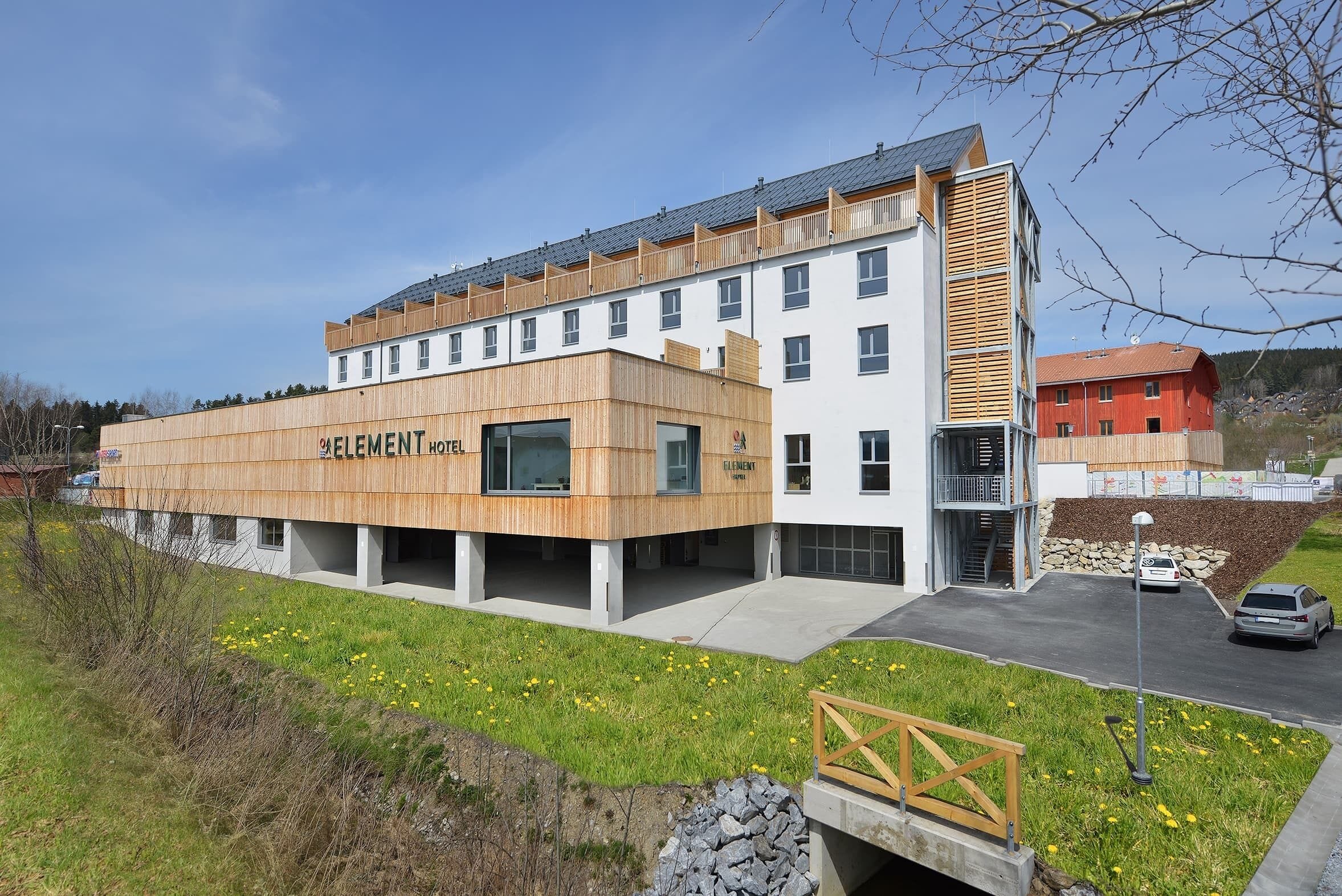 A modern hotel with a wooden facade, multiple floors, and a parking area.