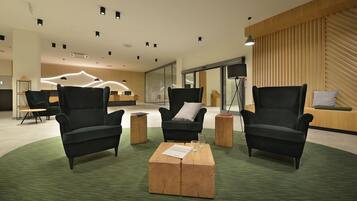 Un moderno vestíbulo con sillones negros, una mesa de centro de madera y una alfombra verde.