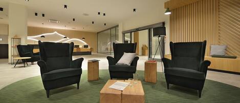 A modern lobby with black armchairs, a wooden coffee table, and a green carpet.