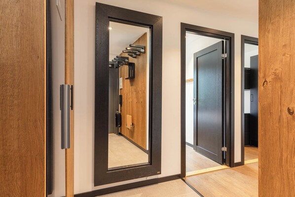 A hallway with wooden doors and a mirrored wall reflecting a staircase.