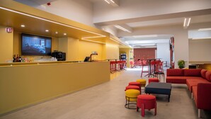 A modern hotel lobby with a bar area, seating, and a large screen displaying 'HOSTEL'. - WOT Nomad Social (Lisbon)