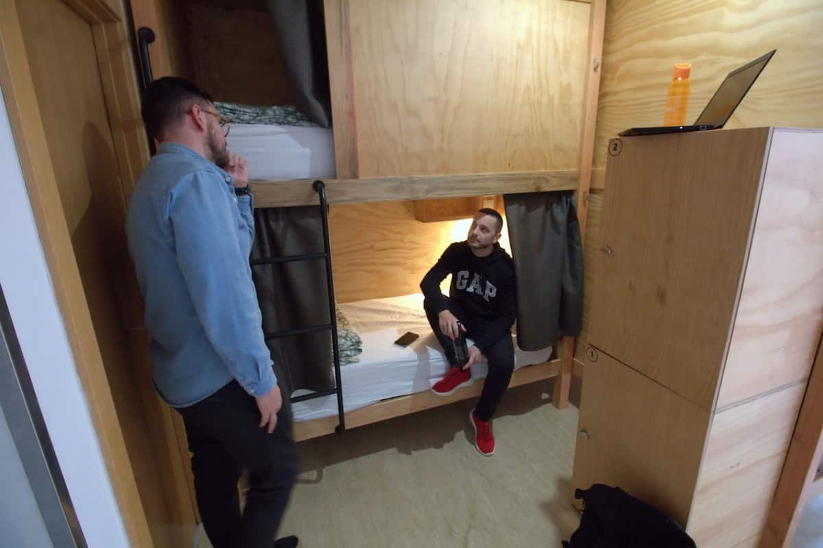 Quarto pequeno e compacto com cama de solteiro, armário de madeira e um laptop em cima do armário.