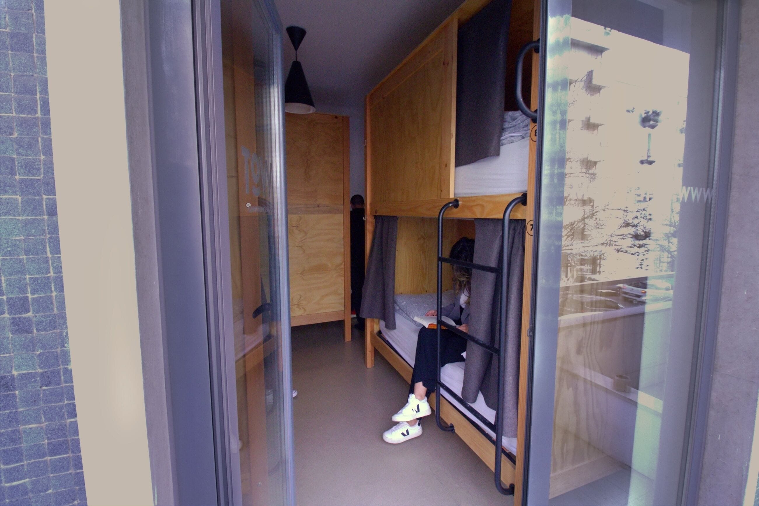 Habitación tipo dormitorio con literas, un vidrio y un pequeño escritorio de madera.