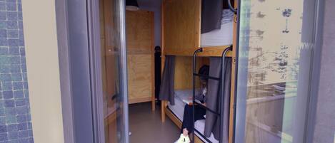Habitación tipo dormitorio con literas, un vidrio y un pequeño escritorio de madera.