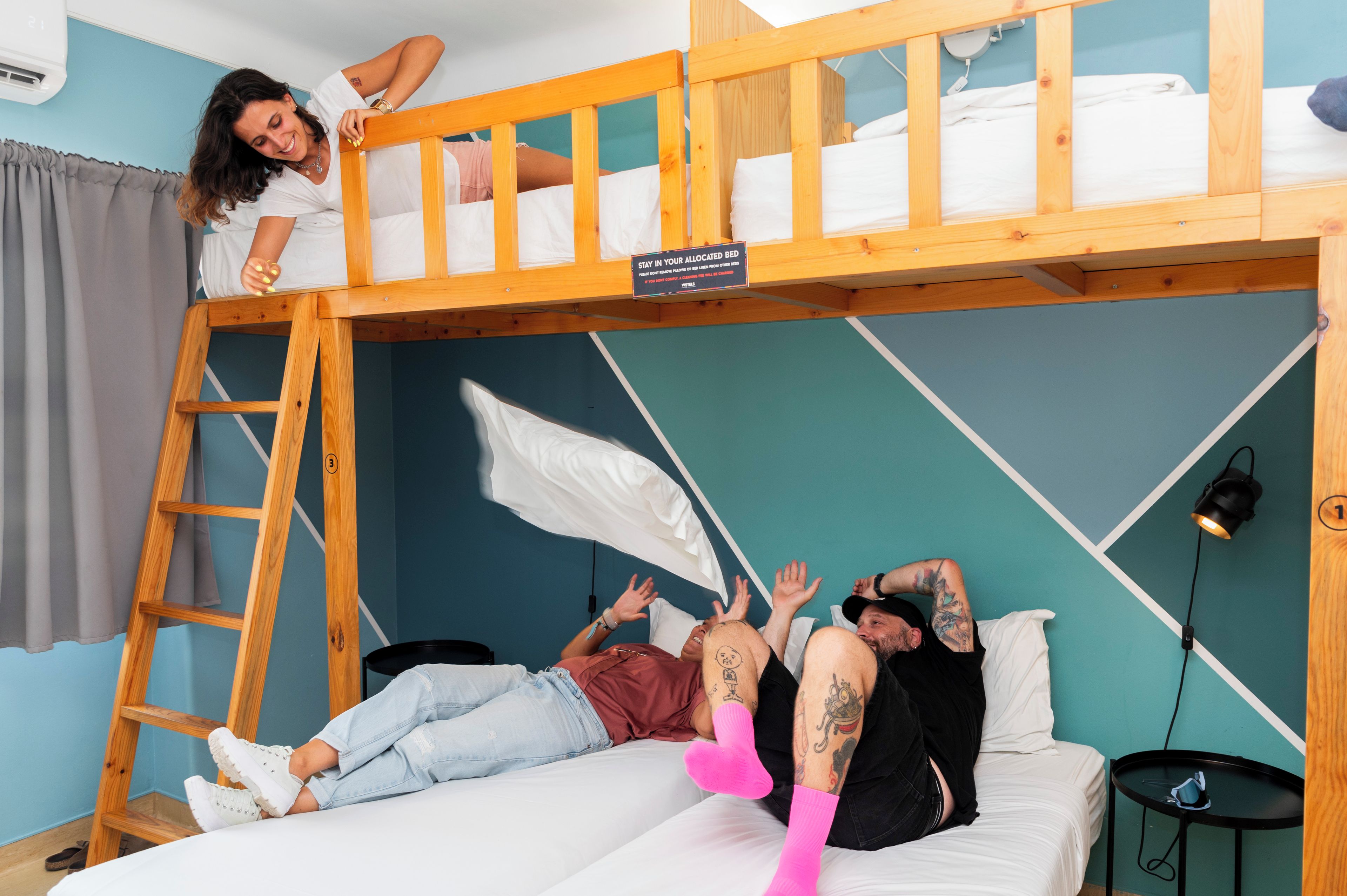A bunk bed with a sign indicating it is an allocated bed, a ladder, and a small table with a cup.