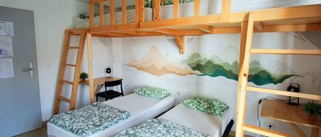A dormitory room with bunk beds, a ladder, a desk, and a wall mural.