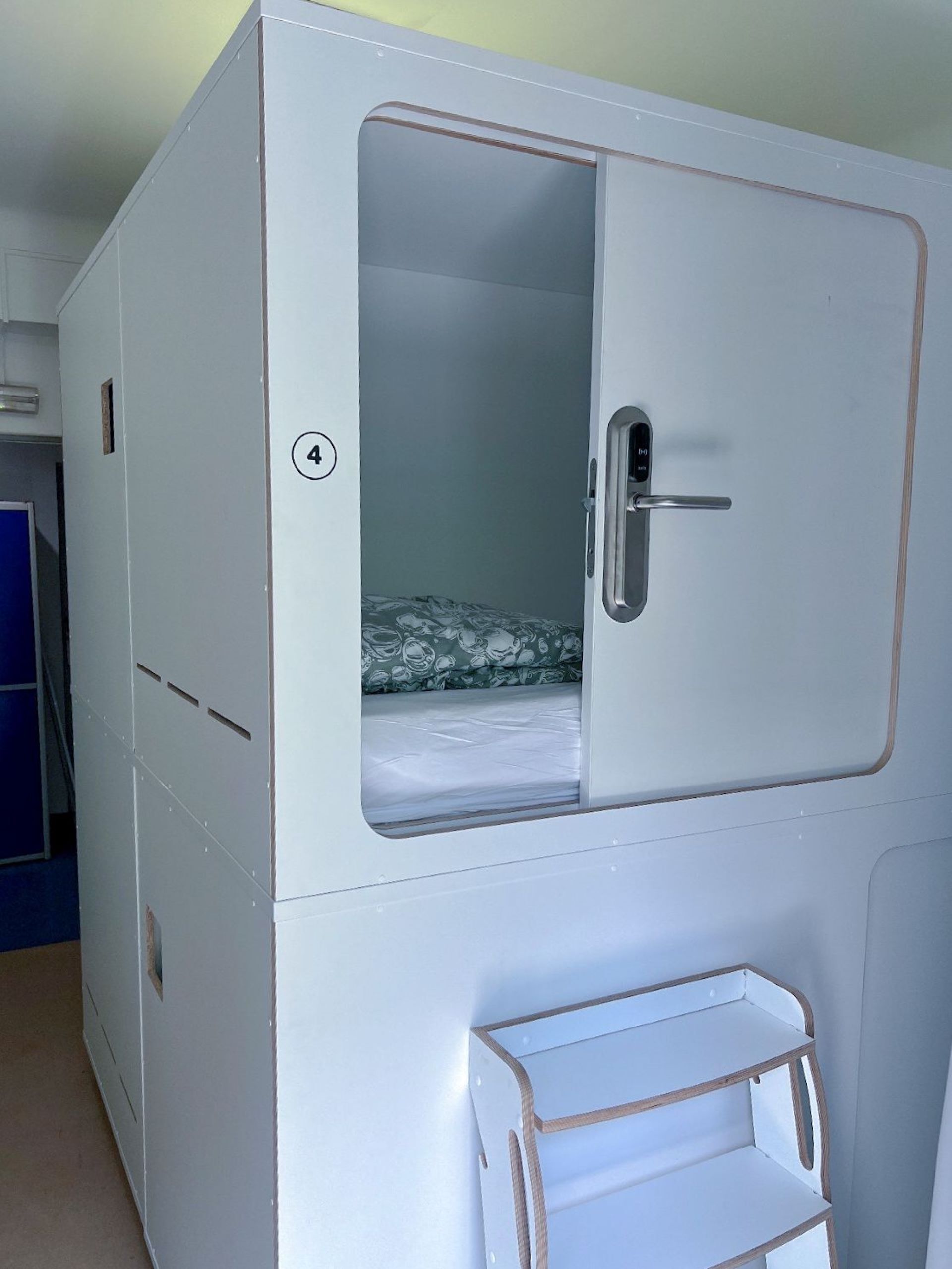 A white room with a bunk bed, a door with a handle, and a small shelf.