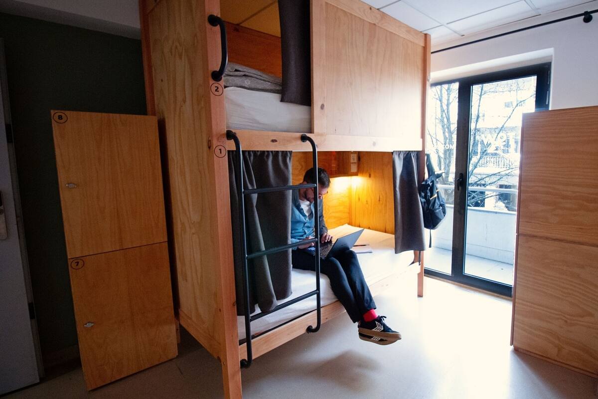 Quarto com beliche, com uma pessoa sentada na cama de baixo usando um laptop.
