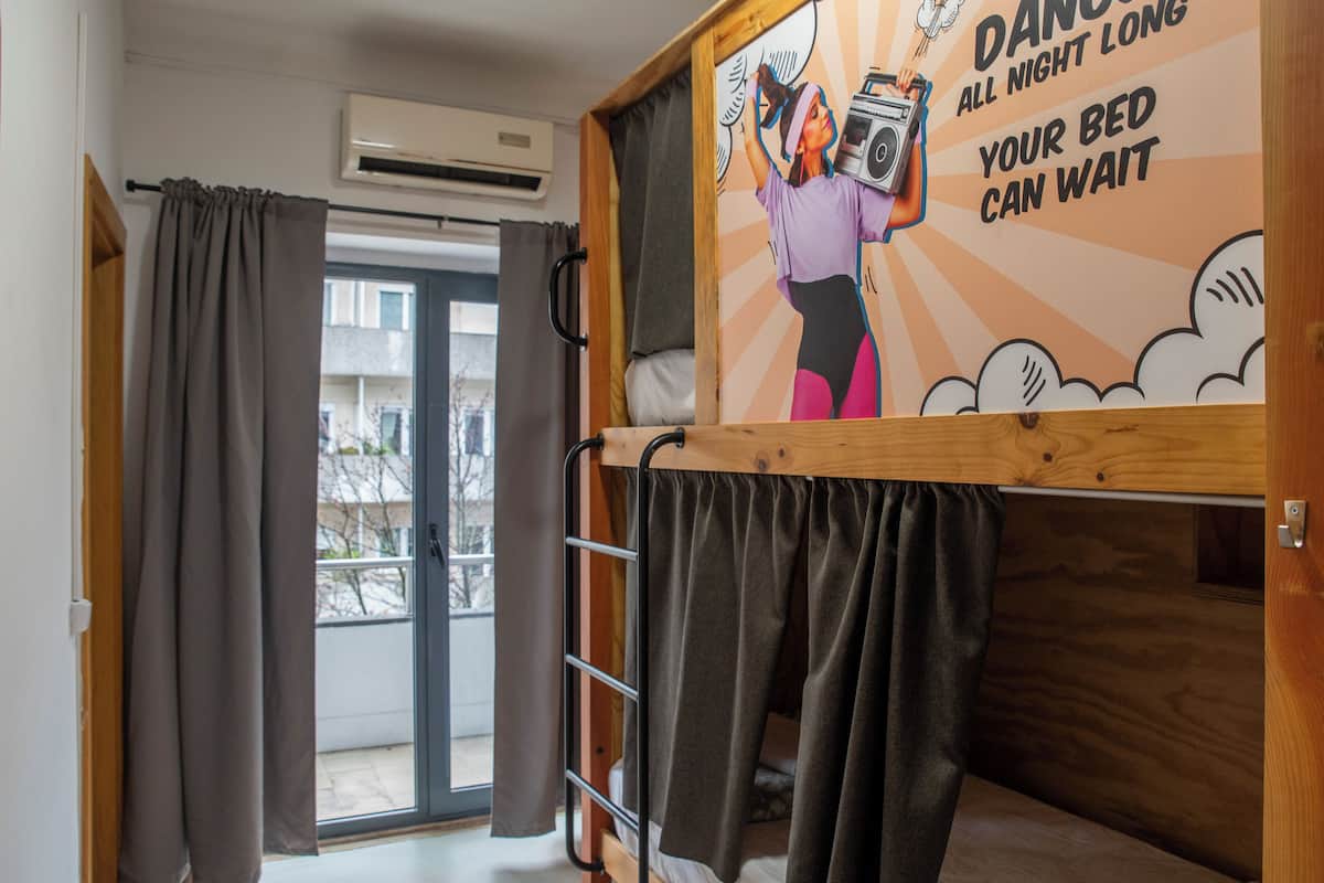 Um quarto de estudante com uma cama de beliche, um mural na parede, uma janela com cortinas e um aparelho de ar condicionado.