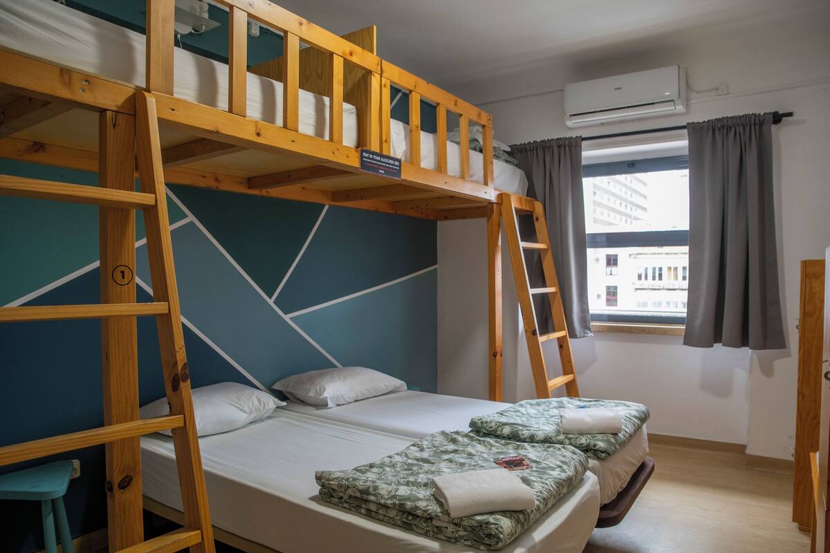 Quarto com beliche, escrivaninha e janela com cortinas.