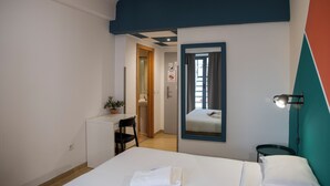 Habitación de hotel con cama, escritorio, silla, mesita, planta en maceta, espejo y ventana con cortinas.