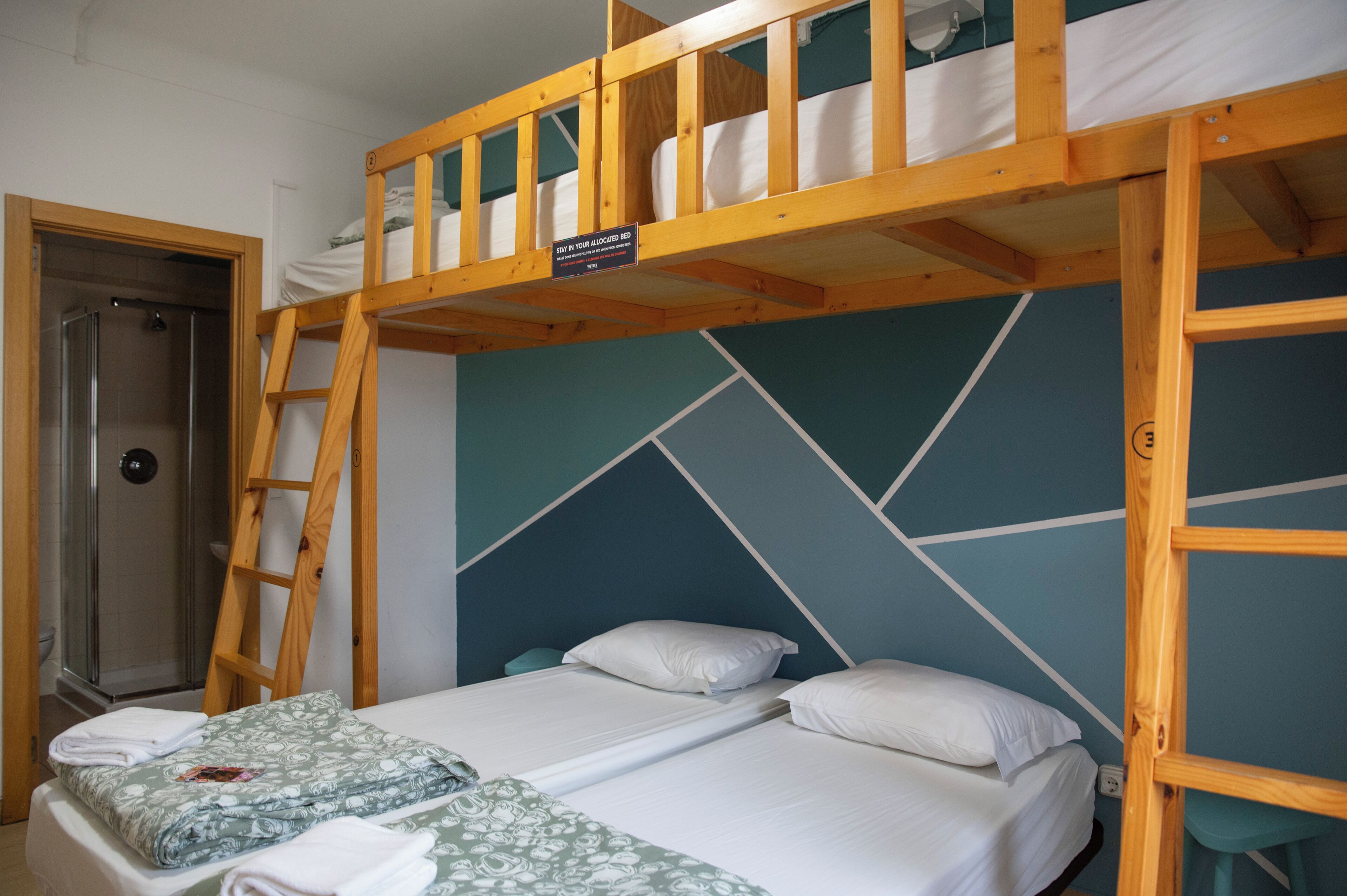 A bunk bed room with a shower, a wooden ladder, and a geometric wall design.