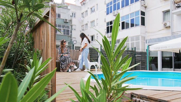 Una terraza de madera con piscina, rodeada de follaje y una cerca.