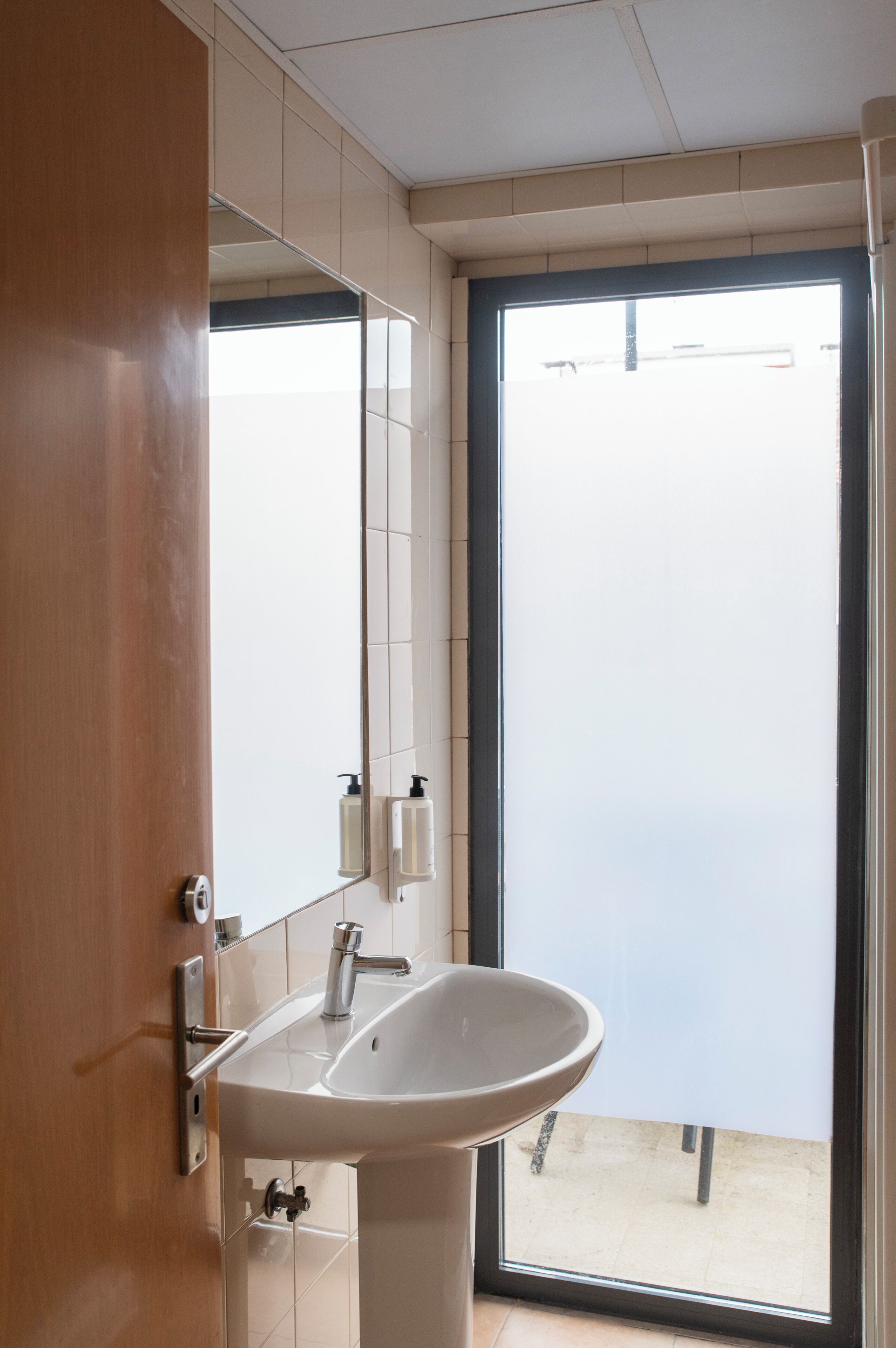 Baño con lavamanos, espejo y puerta que da a un espacio exterior.