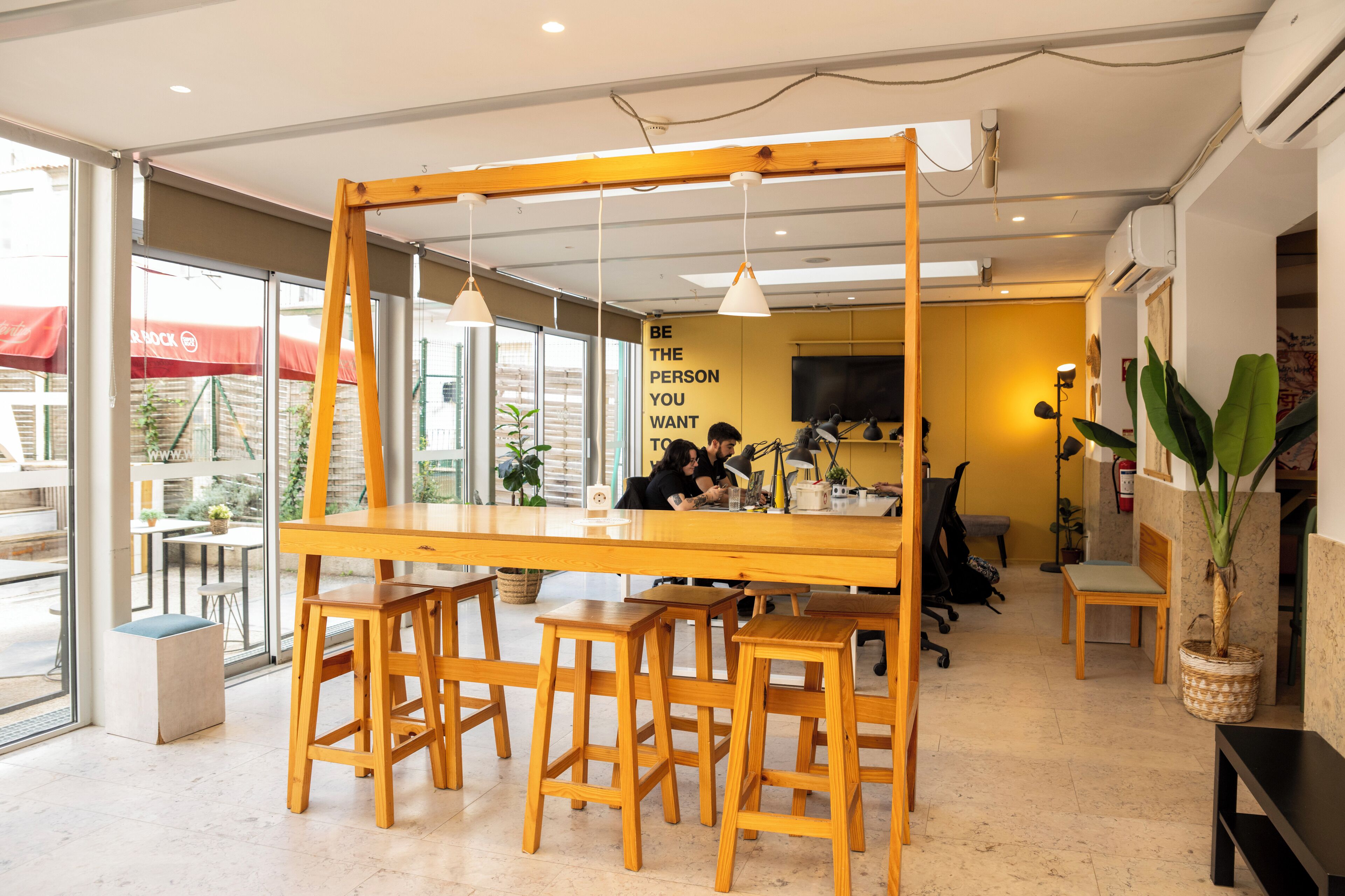 Un espace de travail moderne doté d’une longue table en bois, de plusieurs tabourets et d’un éclairage suspendu.