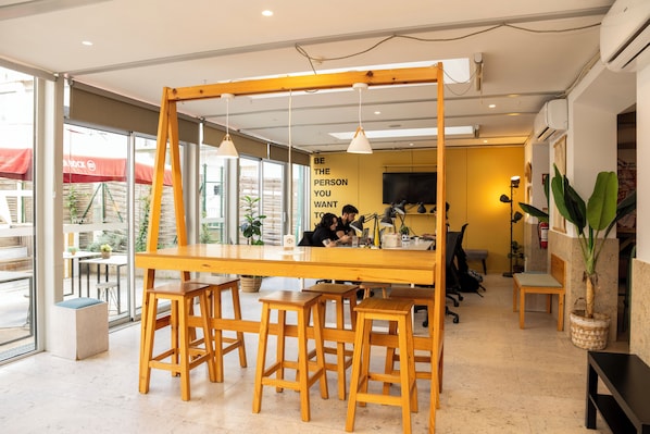 Un espacio de trabajo moderno con una larga mesa de madera, varios taburetes e iluminación colgante.