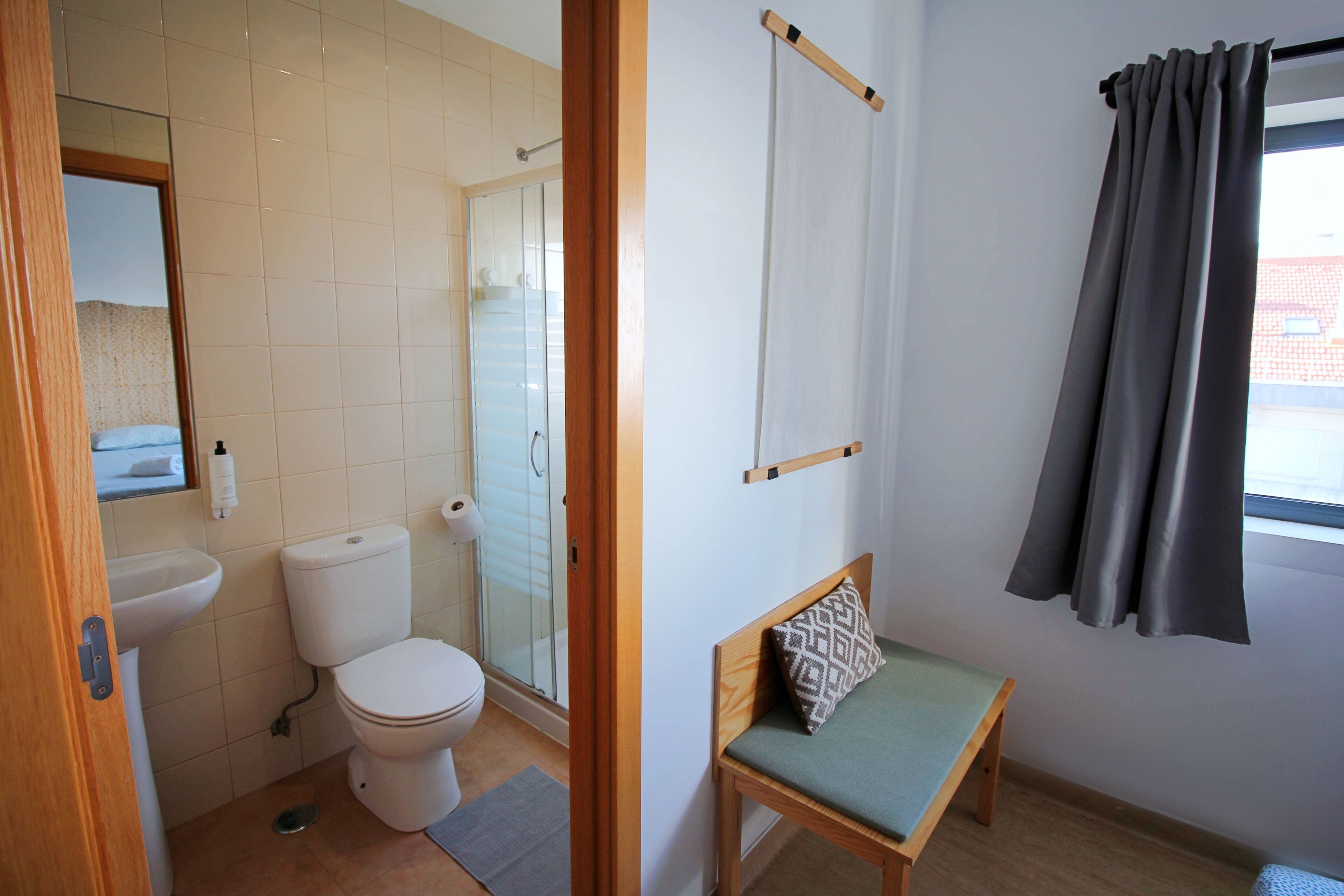 Un bagno con il water, un lavandino e una doccia. Si vede una sedia di legno con un cuscino.