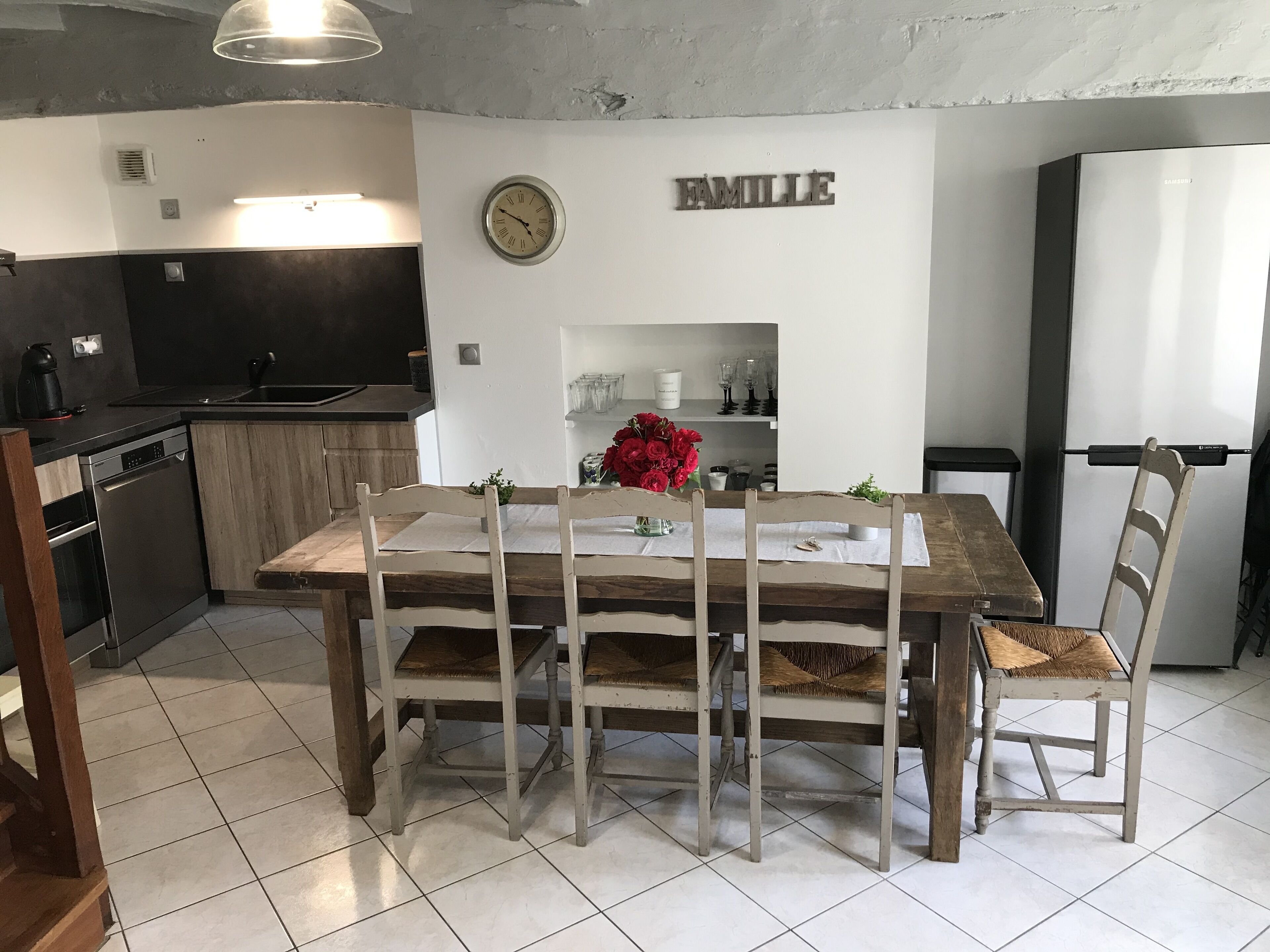 A modern kitchen with a wooden dining table, chairs, and a clock on the wall.