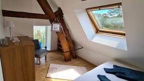Une chambre mansardée chaleureuse, avec un plafond en pente, un bureau en bois, une chaise, une petite fenêtre et une vue sur la verdure.