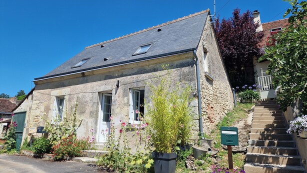 Une maison en pierre avec un toit en pente, une porte d’entrée et un petit porche.