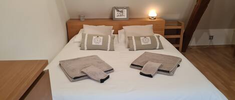 A neatly made bed with white linens, two beige towels, and a framed picture on the headboard.