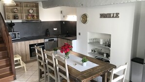 Une cuisine avec des meubles en bois, une table à manger avec des chaises, une horloge et un panneau indiquant « FAMILLE » sur le mur.