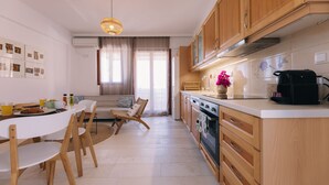 Eine moderne Küche mit Holzschränken, eine Essecke mit weißem Tisch und Stühlen sowie ein großes Fenster mit Vorhängen.