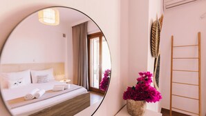 Ein Hotelzimmer mit einem großen Bett, einem Nachttisch mit Blumen in einer Vase, einem Spiegel, der den Raum reflektiert, und einer Holzleiter an der Wand.